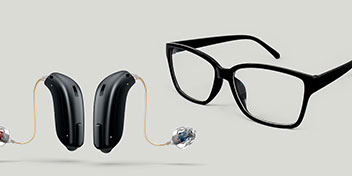 Billedet viser et sæt høreapparater og nogle briller.