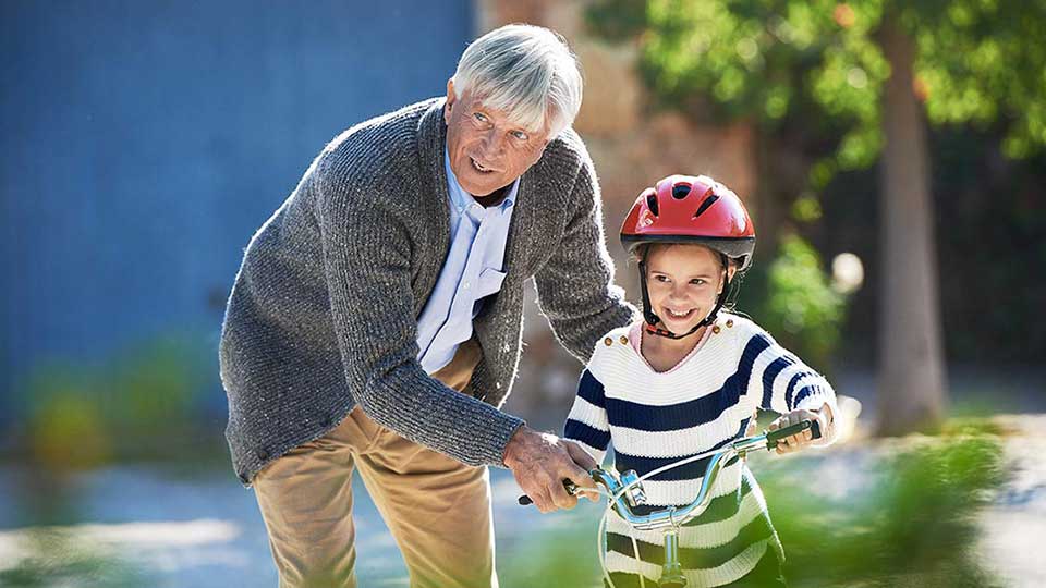 Billedet viser en bedstefar og et barnebarn. Farfaren hjælper barnebarnet med at lære at køre på cykel.
