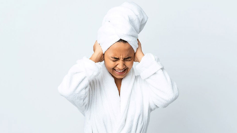 mujer joven con toalla en la cabeza tocando los oídos con dolor 