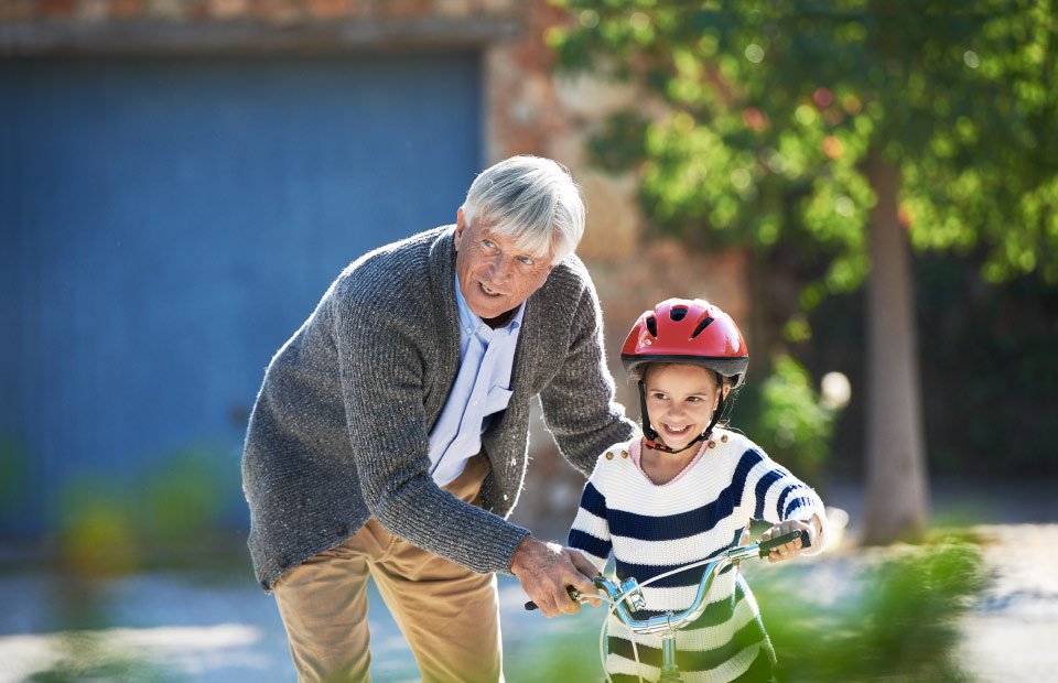 abuelo con audífonos ayudando a su nieta a andar en bici