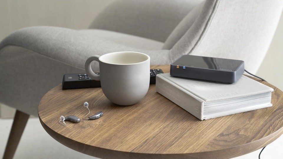 Des appareils auditifs mini-contours posés sur une table de salon à côté d'une tasse