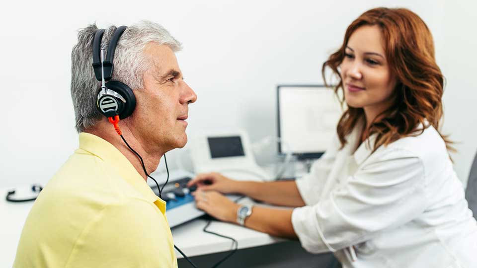 Homme portant un casque auditif passant un test auditif avec une audioprothésiste