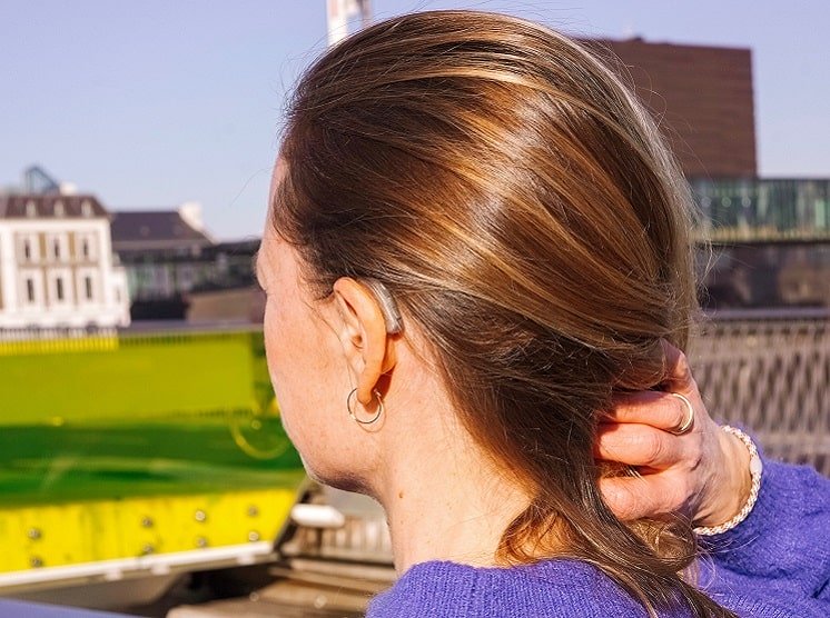 Une femme de profil avec un appareil auditif mini-contours qui se tient les cheveux 