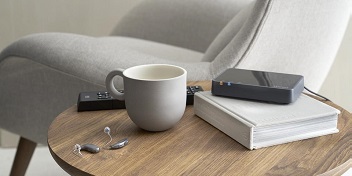 Des appareils auditifs mini-contours posés sur une table de salon à côté d'un livre et d'une tasse
