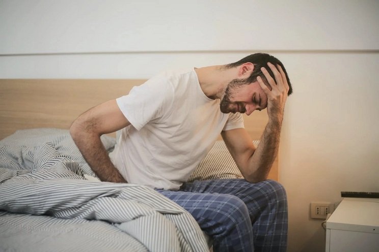 Un homme se tient la tête en sortant du lit car il souffre d'acouphènes après avoir été à un concert