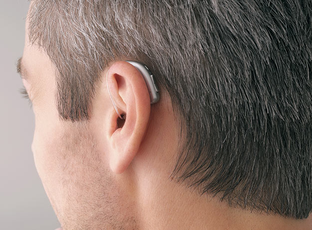 Un homme de profil aux cheveux grisonnants portant des appareils auditifs