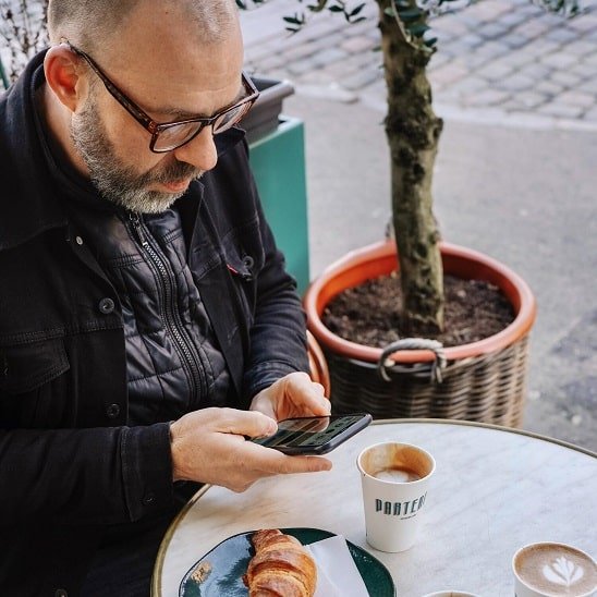 Un client Audika sur une terasse de café qui met un avis sur son téléphone