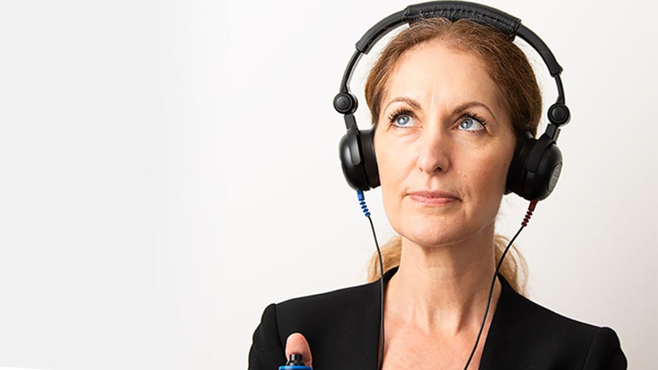 Bild på en kvinna som har hörlurar och gör en gratis hörselkoll hos Audika där hon får en indikation på hur hon hör