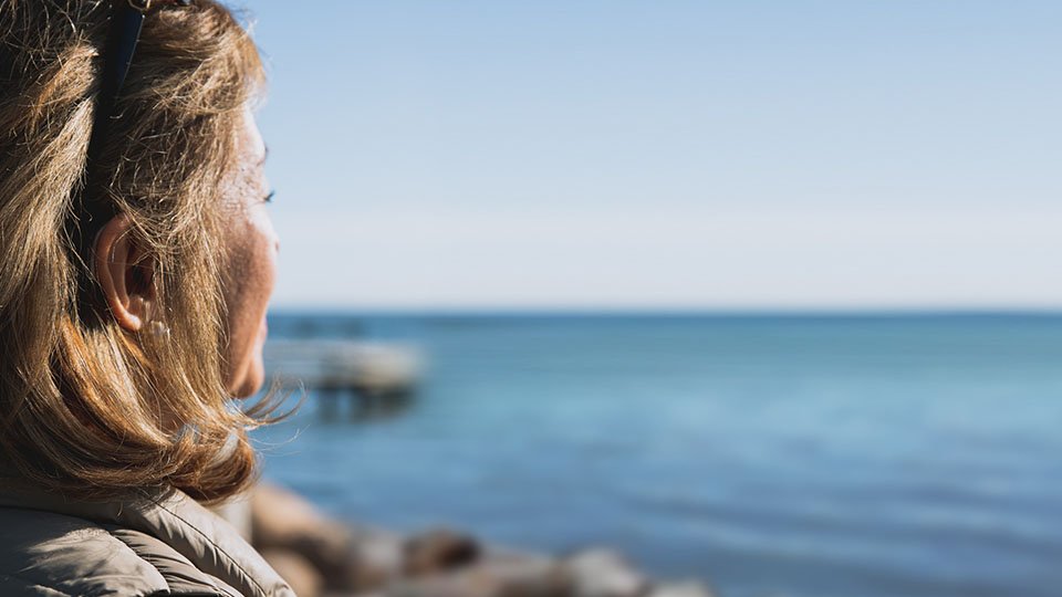 Bild på kvinna som med hörapparat som blickar ut mot havet