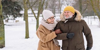 Bild på ett par som är vinterklädda och går igenom en snöig park