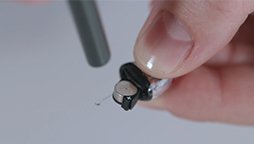 Bild på en hand som visar ett användningstips på hur man byter batteri i en allt-i-örat hörapparat