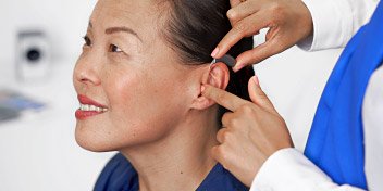 Bild på hörapparat som placeras på en kvinnas öra. Kvinnan är kund till Audika.