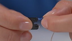 Bild på ett par händer som byter produkt på hörapparat som har ljudslang