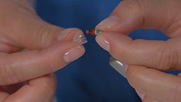 Bild på ett par händer som byter produkt på hörapparat med vaxfilter