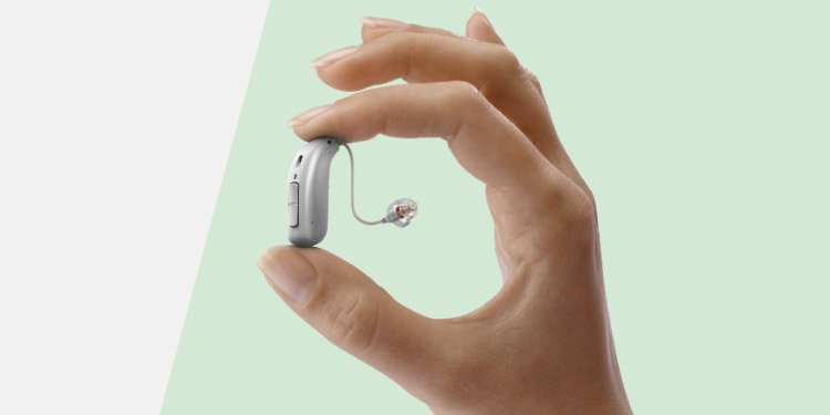 En hand som håller i en hörapparat som kan anslutas till ett hörselhjälpmedel.