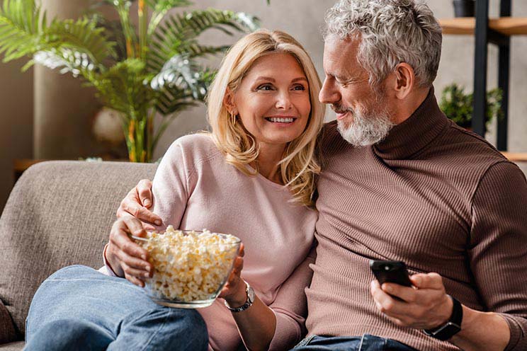 Par som har hörapparater med Bluetooth, äter popcorn och tittar på TV.