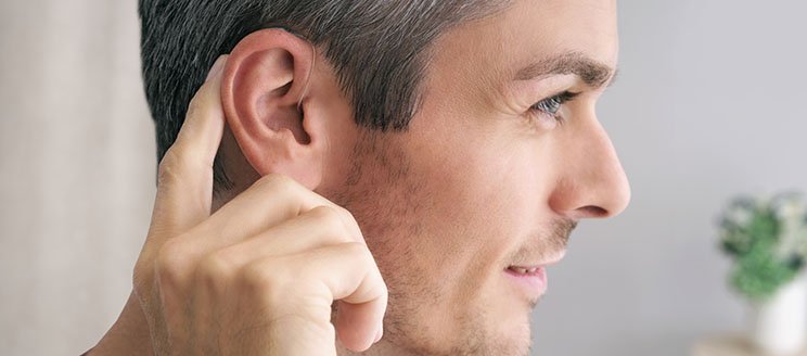 Bild på man som har en ny hörapparat på bakom örat. Mannen pekar på örat och han visas i profil.