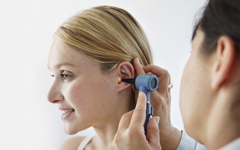 Bild på audionom som tittar i örat på kund som vill testa hörselskydd.