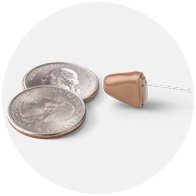 Bild på en hörapparat och två mynt som jämför storleken på hörapparaten