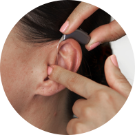Bild på en audionoms hand som sätter i ett hjälpmedel i en kvinnas öra.