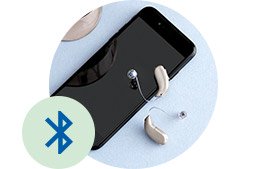 Bild på en iphone och ett par hörapparater som ägs av en hörappatsanvändare