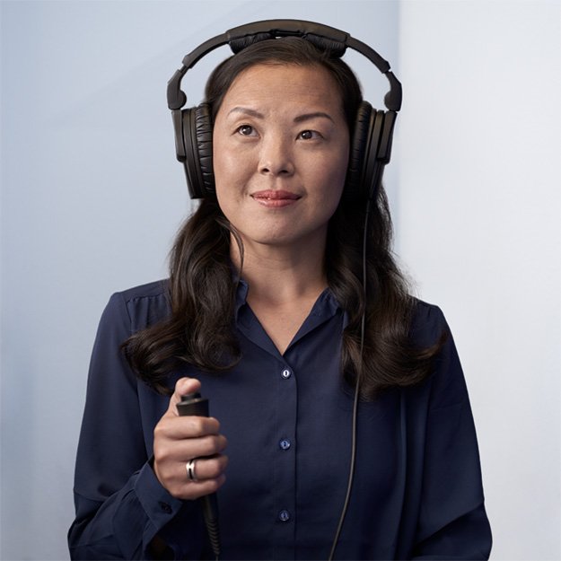 Bild på en kvinna som får hjälp av legitimerade audionomer att göra ett hörseltest på en av Audikas hörselkliniker