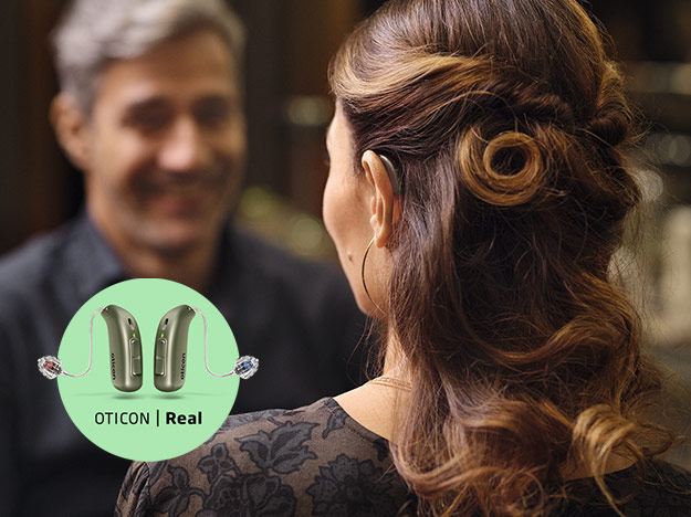 Bild på en kvinna som talar med en man, hon har en Oticon Real hörapparat som hon har provat ut ur Audikas privata sortiment av hörapparater