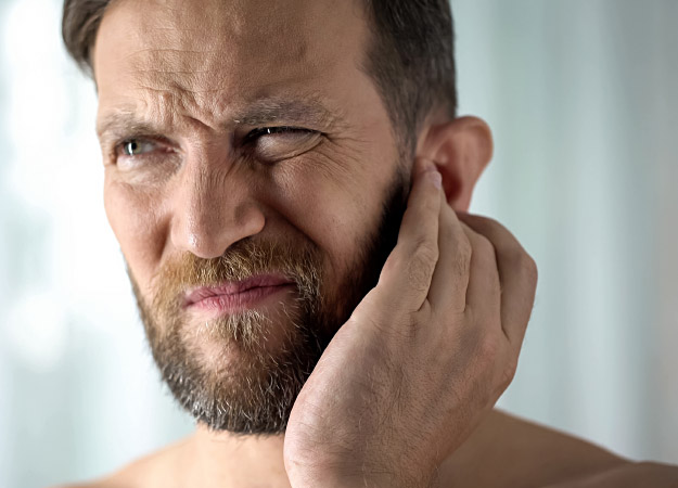 Bild på en man som har tinnitus som tar sig för örat