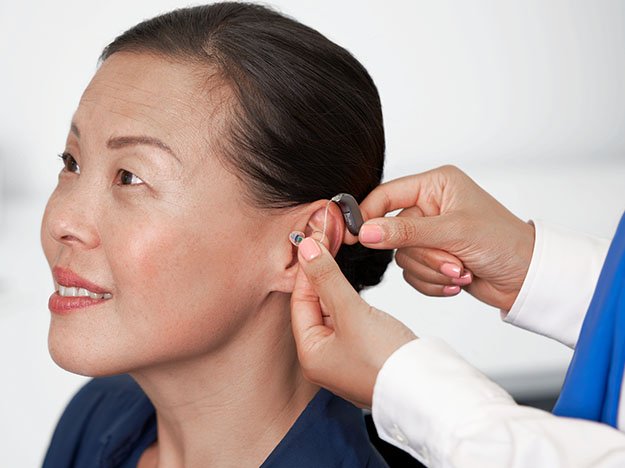 Kvinna som provar ut hörapparat i Skåne. Audionom som sätter i hörapparaten i örat.