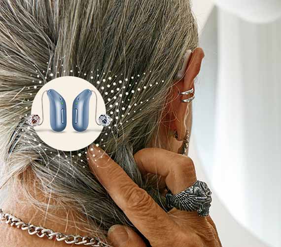 Bild på en kvinna som visar den uppladdningsbara hörapparaten hon har bakom örat, Oticon Intent