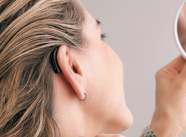 Bild på en kvinna som har symtom på tinnitus som har en hörapparat på sig som kan lindra symtomen