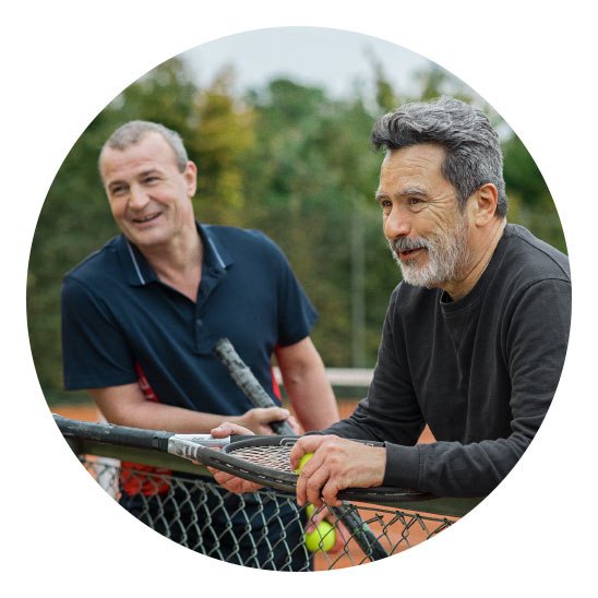 Bild på två män som står vid en tennisbana som älskar sin hörsel och tar hand om sin hälsa för att fortsätta leva ett aktivt liv