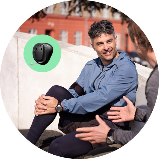 Bild på en man som älskar sina öron och sitter och pratar med sin kompis om sin nya hörapparat Oticon Own som man ser på en mindre bild i en grönt ring