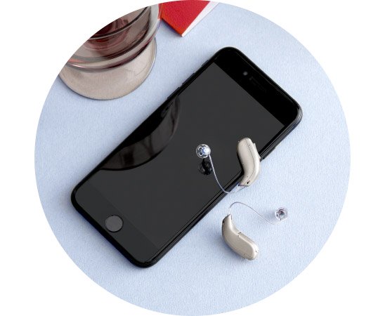 Bild på svart smartphone och bredvid ligger två silverfärgade hörapparater.