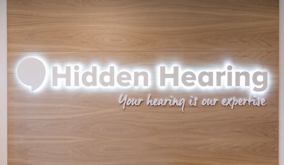 Hidden Hearing Logo in clinic shining against a wooden background
