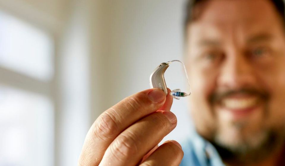 Man holding a hearing aid up while smiling in the background