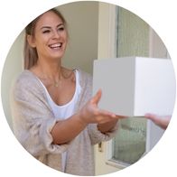 A woman with her door open who has a smile on her face after receiving a box in a delivery 