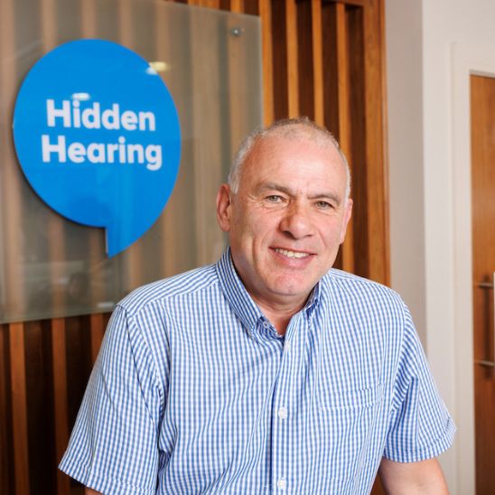 Irish rugby legend Tony Ward smiling happily in front of Hidden Hearing signage