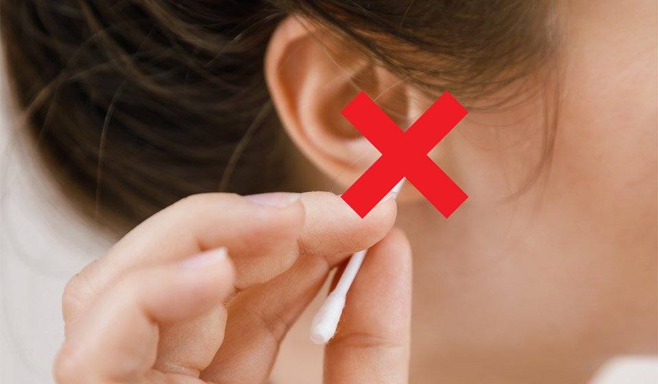 Image shows a girl with a cotton swab in her ear and a red cross over the cotton swab