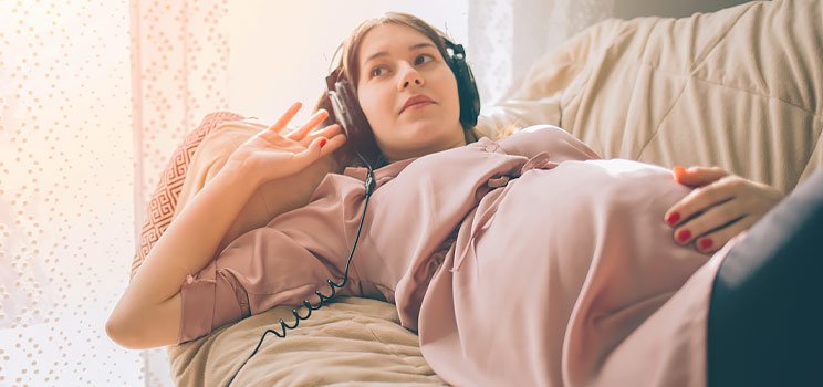 Image shows a pregnant woman listening to music