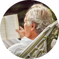 Image shows a man reading in the garden wearing a digital hearing aid