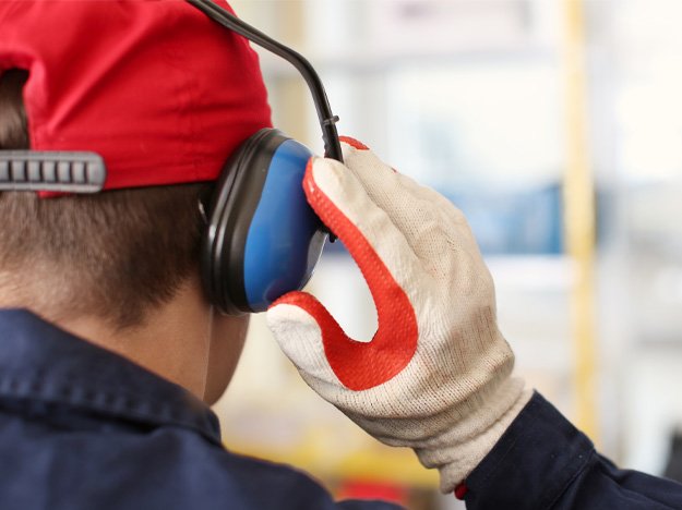 Image shows a man protecting his ears from loud industrial noise