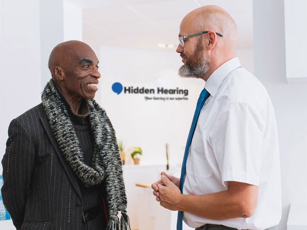 Images shows a Hidden Hearing audiologist talking to a customer