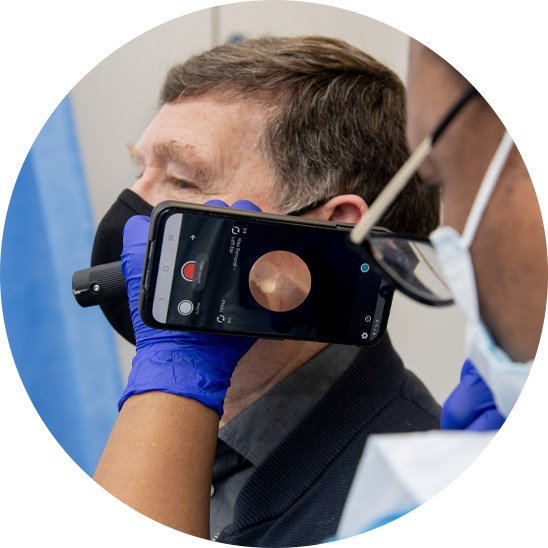 Image shows a hearing specialist removing the wax from a patient's ear