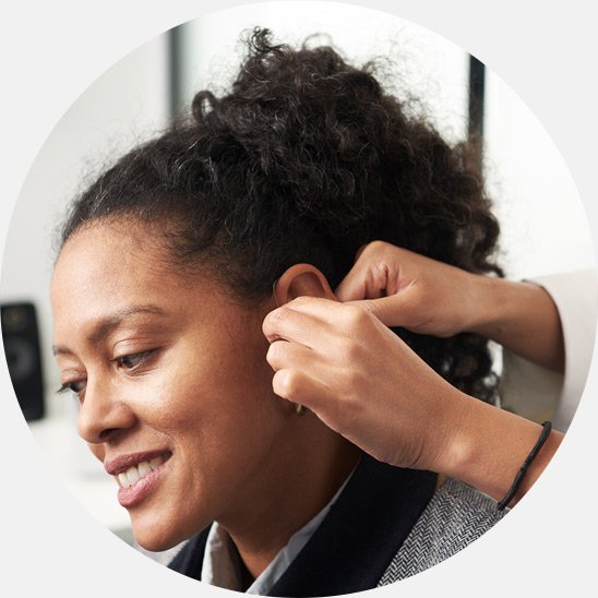 Image shows a dispenser fitting a hearing aid on a woman's ear