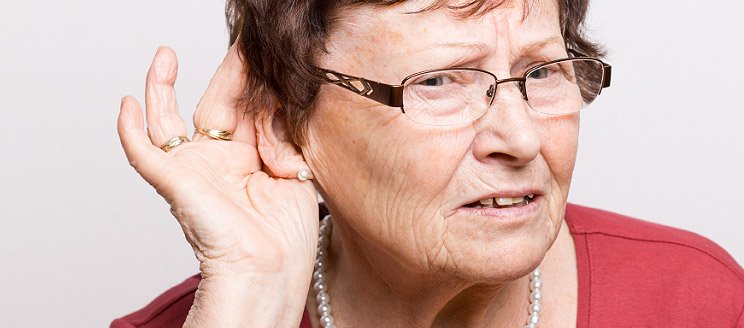 Image shows elderly lady holding hand close to ear to hear better