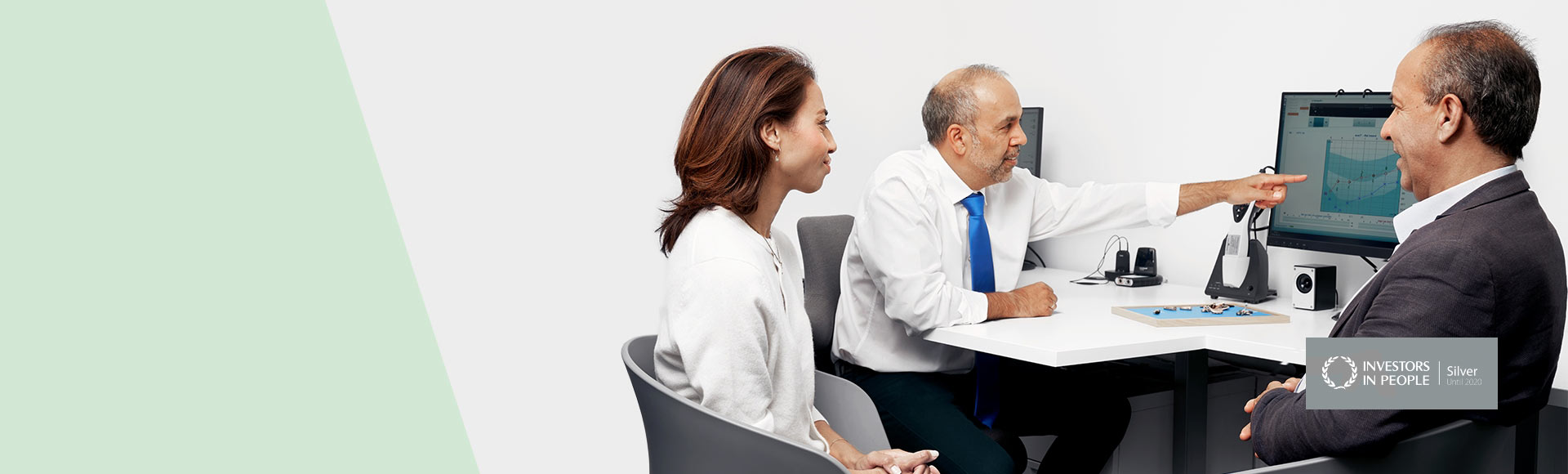 Image shows couple in hearing clinic with audiologist in front of screen with audiogram