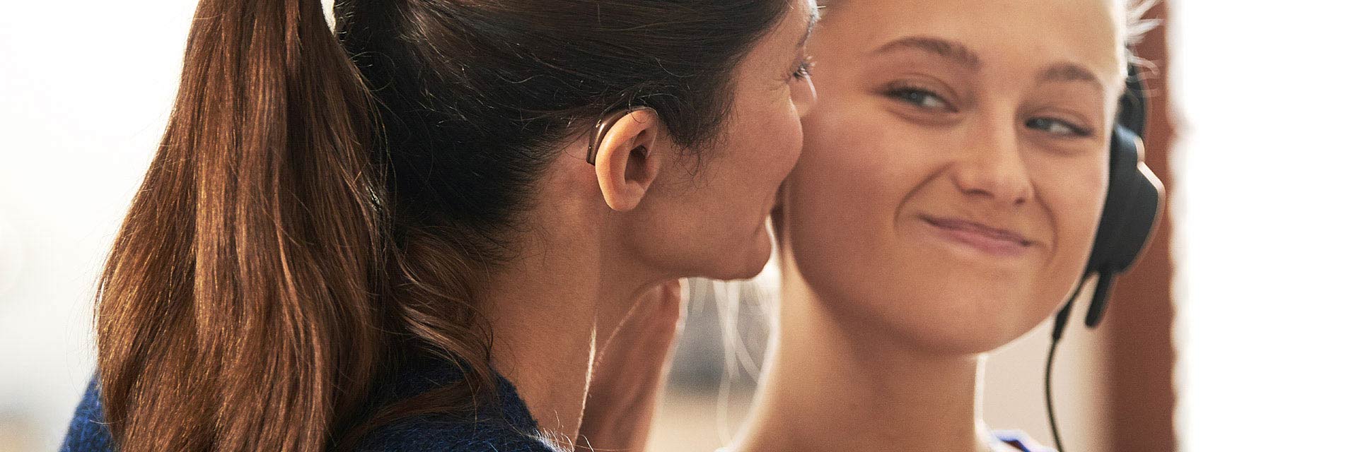 Immagine di una donna con un apparecchio acustico nell'orecchio e di una ragazza che sorridono l'una con l'altra. 