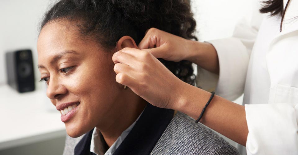 Imagem mostra audiologista a colocar aparelhos auditivos no ouvido de uma mulher 