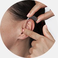 La imagen muestra una mano colocando un audífono en el oído